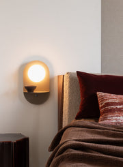 It's about RoMi Wandleuchte Tokyo: Beige Wandleuchte mit rundem Glasschirm, im Schlafzimmer neben einem Bett montiert.