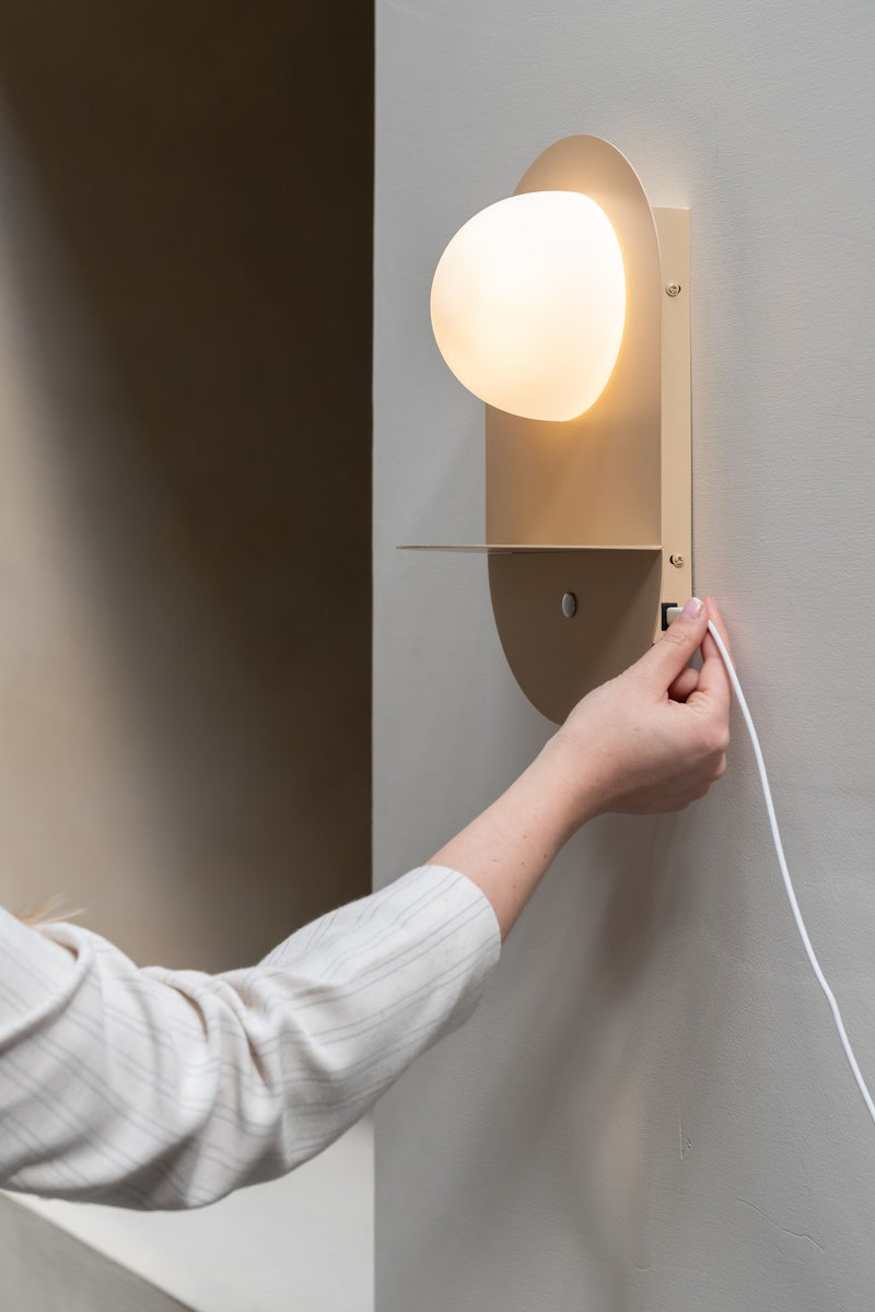 Wandleuchte RoMi Tokyo: Beige Wandleuchte mit rundem Glasschirm und Metallgestell, daneben eine Ablage.
