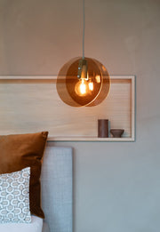 Pendelleuchte It's about RoMi Toledo mit zwei bernsteinfarbenen Glasscheiben über einer Glühlampe, vor einer hellen Holzwand.