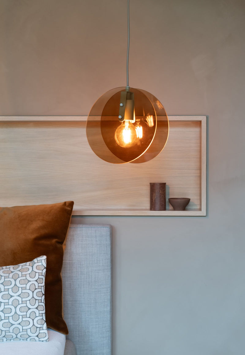 Pendelleuchte It's about RoMi Toledo mit zwei bernsteinfarbenen Glasscheiben über einer Glühlampe, vor einer hellen Holzwand.