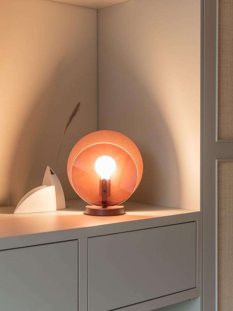 Runde Glas-Tischleuchte RoMi Toledo in Bernstein-Braun mit sichtbarer Glühbirne auf einem Sideboard, warmes Licht.