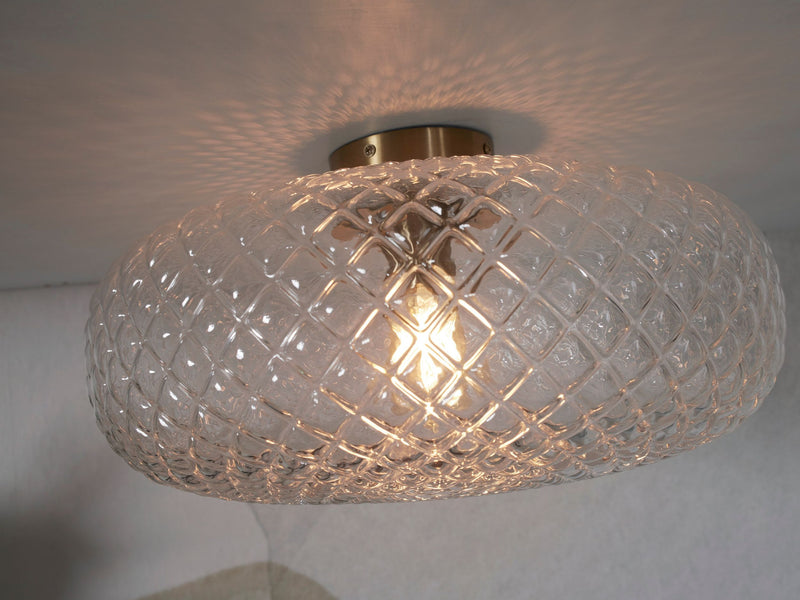 Deckenleuchte RoMi Venice aus klarem, geripptem Glas mit goldfarbenem Metallteller, eingeschaltet, mit Lichtreflexen an der Decke.