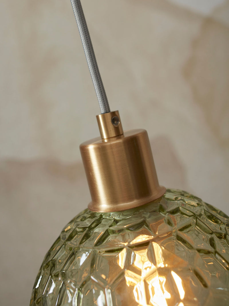 Detailansicht der grünen Hängeleuchte Venice mit facettiertem Glasschirm und goldfarbenem Metallbaldachin am grauen Textilkabel.