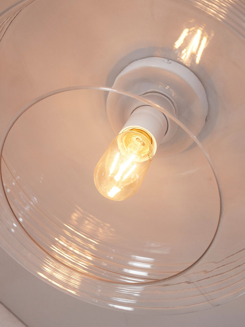 Detailansicht der RoMi Deckenleuchte Verona aus Glas mit klarem Glasschirm und brennender Glühlampe.