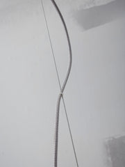 Detailaufnahme eines grau-weiß geflochtenen Hängeleuchten-Kabels, das an einem Verbindungsstück über einer hellen Wand zusammenläuft.