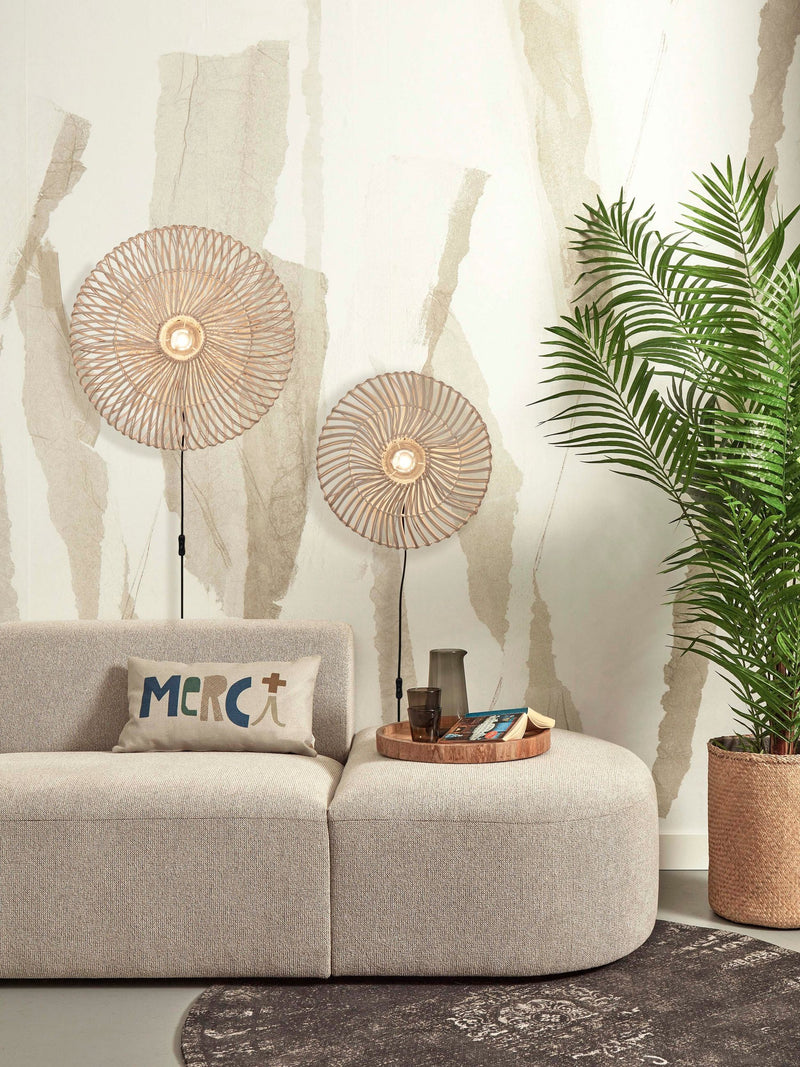 Zwei runde Wandleuchten aus Rattan mit Eisengestell an einer hellen Wand, daneben ein Sofa in Beige und eine Zimmerpalme.