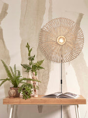 Good&Mojo Wandleuchte Zanzibar aus Rattan mit rundem, geflochtenem Schirm an weißer Wand, daneben Pflanzen auf einer Konsole.