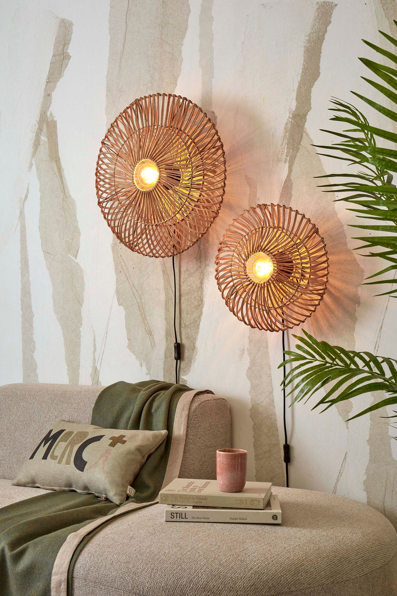 Zwei runde Wandleuchten aus Rattan in Naturtönen mit sichtbarem Geflecht, eingeschaltet über einem Sofa.