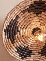 Detailansicht der Good&Mojo Deckenleuchte Andros aus spiralförmig geflochtenem Seegras in Schwarz und Natur, mit eingeschalteter Glühlampe.