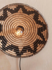 Wandleuchte Andros aus Seegras in Schwarz und Natur, Detailansicht des spiralförmig geflochtenen Schirms mit eingeschalteter Glühbirne.