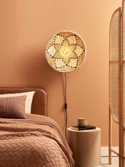Runde Wandleuchte Andros aus Seegras in Natur/Weiß, an der Wand im warm getönten Schlafzimmer eingeschaltet.