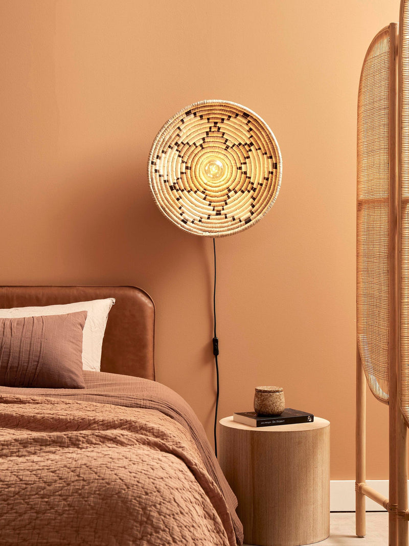 Runde Wandleuchte Andros aus Seegras in Natur/Weiß, an der Wand im warm getönten Schlafzimmer eingeschaltet.