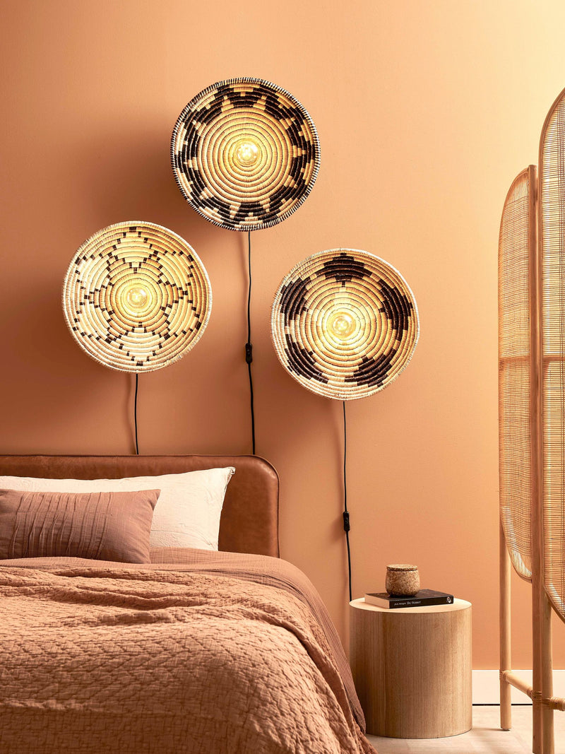 Drei runde Wandleuchten aus Seegras mit dunklen Mustern hängen an einer terrakottafarbenen Wand über einem Bett.