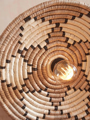 Detailansicht der Wandleuchte Good&Mojo Andros aus Seegras: spiralförmig geflochtener Schirm mit schwarzen Akzentstreifen, leuchtende Glühbirne.