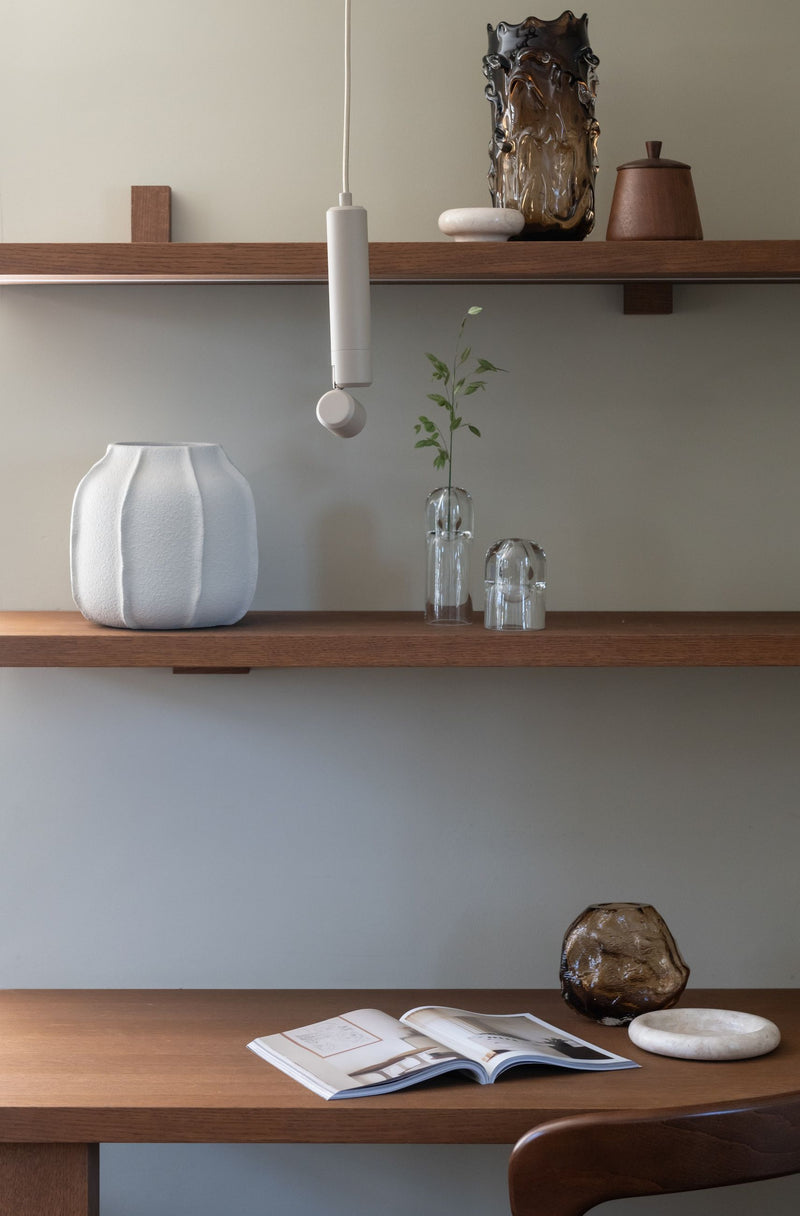 Hängeleuchte Milan in Sand mit Aluminiumschirm, im Vordergrund über einem Holzregal mit weißer Vase und Glasobjekten.