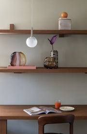 Hängeleuchte It's about RoMi Murano mit mattweißem Glasschirm und Eisengestell, über einem Holzregal mit Vasen und Schalen.