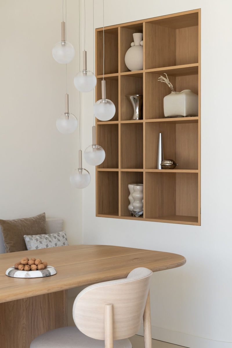 Sechs weiß-milchige Glaskugeln hängen in unterschiedlichen Höhen von der Decke über einem Esstisch aus hellem Holz.