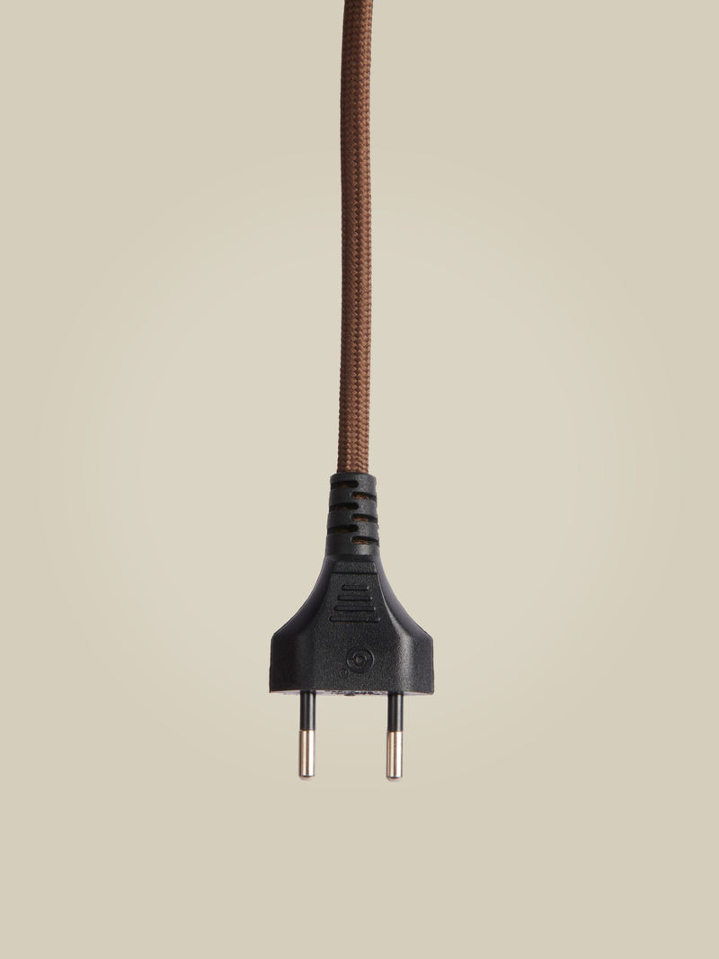Detailansicht des braunen, textilummantelten Netzkabels mit schwarzem Euro-Stecker vor neutral beigem Hintergrund.