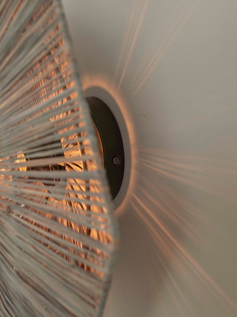 Detailansicht der Wandleuchte Panama von Good&Mojo: geflochtener Raffia-Schirm mit warmem Lichtschein an dunkler Eisen-Halterung.