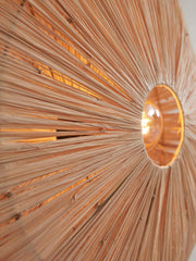 Detailansicht der Raffia-Deckenleuchte Panama von Good&Mojo: radial angeordnete Raffiafasern, eingeschaltetes Leuchtmittel in der Mitte.