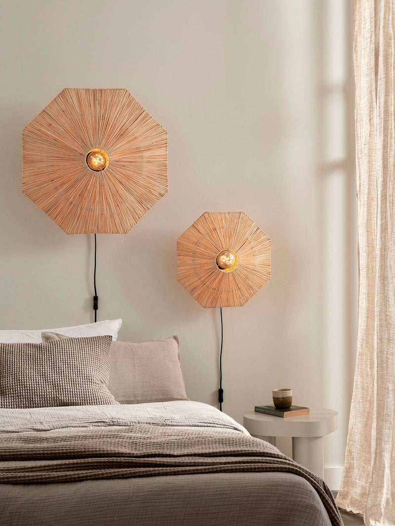Zwei achteckige Wandleuchten Panama aus geflochtenem Raffia in Naturbraun über einem Bett, unterschiedlich groß.