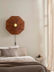Good&Mojo Wandleuchte Panama aus Raffia: achteckiger, brauner Schirm mit eingeschaltetem Leuchtmittel über einem Bett.