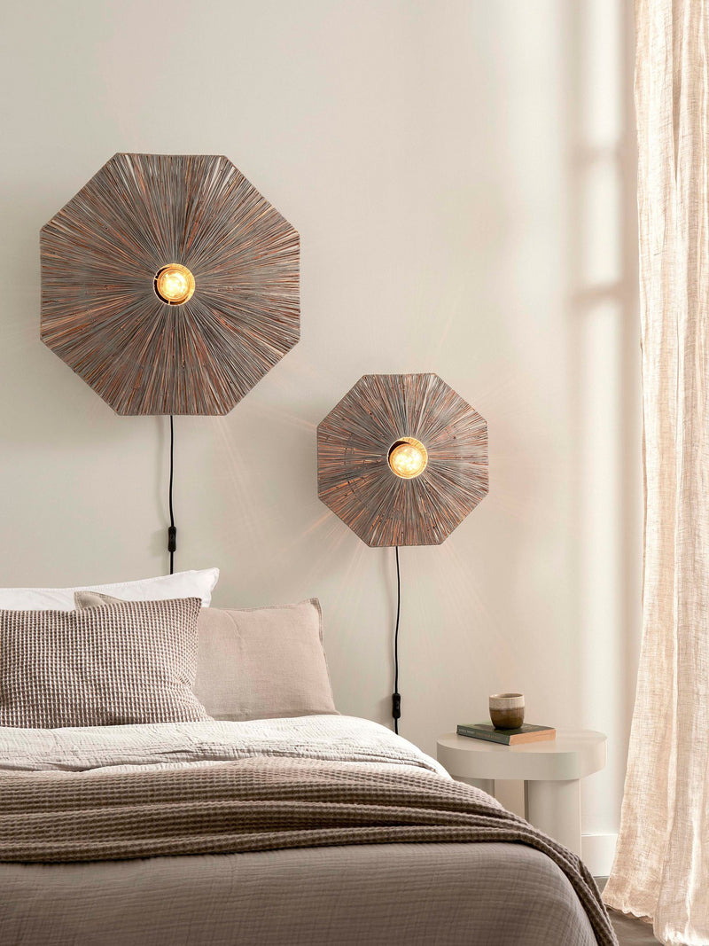 Good&Mojo Wandleuchte Panama aus Raffia: zwei achteckige Wandleuchten mit braunem, strahlenförmig geflochtenem Schirm über einem Bett.