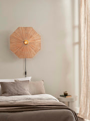Good&Mojo Wandleuchte Panama aus Raffia: achteckiger, sternförmig geflochtener Schirm über dem Bett, seitlich herabhängendes Kabel.