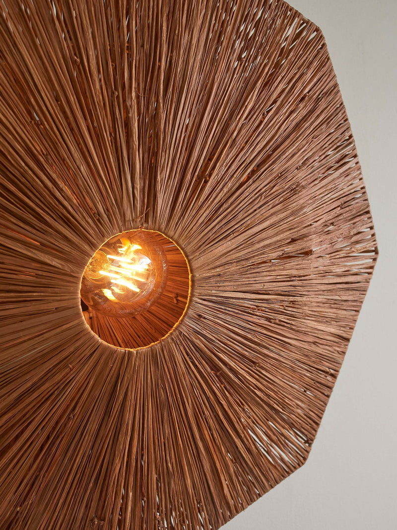 Detailansicht der Good&Mojo Wandleuchte Panama aus braunem Raffia: radial geflochtener Schirm mit leuchtender Glühbirne im Zentrum.